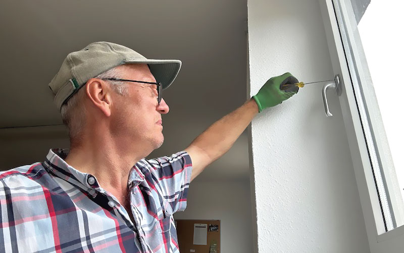 Frank Bär, Geschäftsführer Haus- und Gartenpflege, bringt einen Sicherheitsgriff an einem Fensterrahmen an.